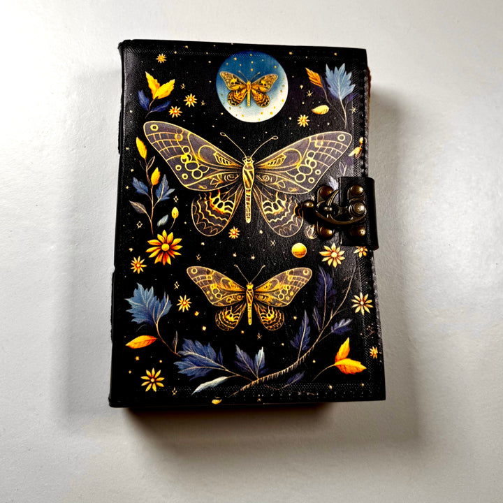 The Goleden Butterfly -muistikirjan etukansi, jossa perhossymboli ja koristeellinen kuviointi. - Front cover of The Golden Butterfly -notebook featuring a butterfly symbol and embossed decorative details.
