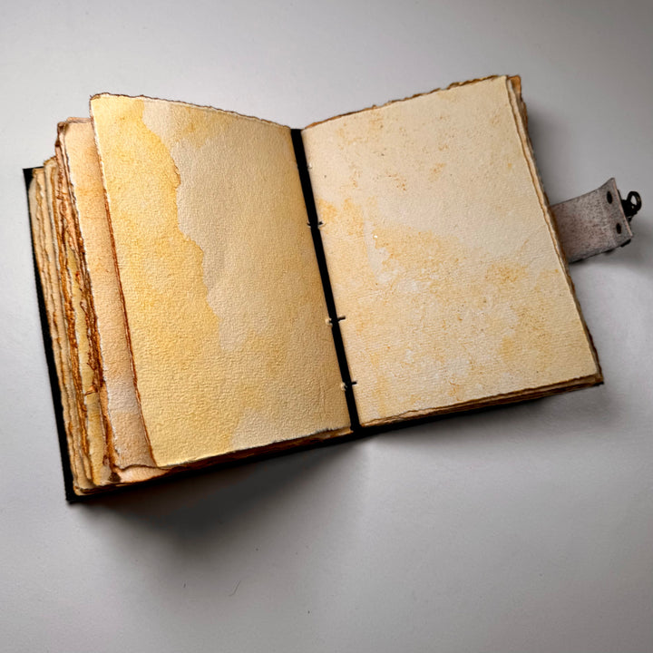 Käsintehty nahkainen muistikirja avattuna – näkyvissä sivuaukeama ja käsintehdyn paperin rustiikkinen tekstuuri. - Handcrafted leather notebook opened – showing a double page spread with the rustic texture of handmade paper.