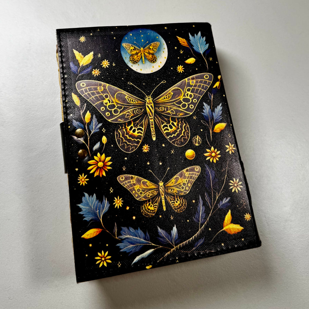 Perhosaiheinen nahkakantinen muistikirja takaa kuvattuna, esillä kirjan takakansi. - Golden Butterfly-themed leather-bound notebook photographed from the back, showing the book’s back cover.