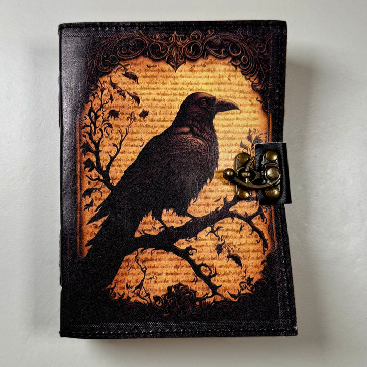 The Raven Grimoire Shadow -muistikirjan etukansi, jossa korppisymboli ja koristeellinen kohokuviointi. - Front cover of The Raven Grimoire Shadow journal featuring a raven symbol and embossed decorative details.