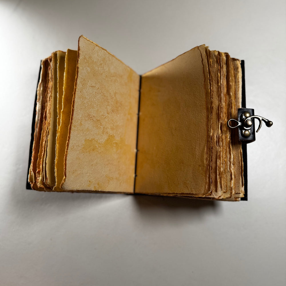 Käsintehty nahkainen muistikirja avattuna – näkyvissä sivuaukeama ja käsintehdyn paperin rustiikkinen tekstuuri. - Handcrafted leather journal opened – showing a double page spread with the rustic texture of handmade paper.