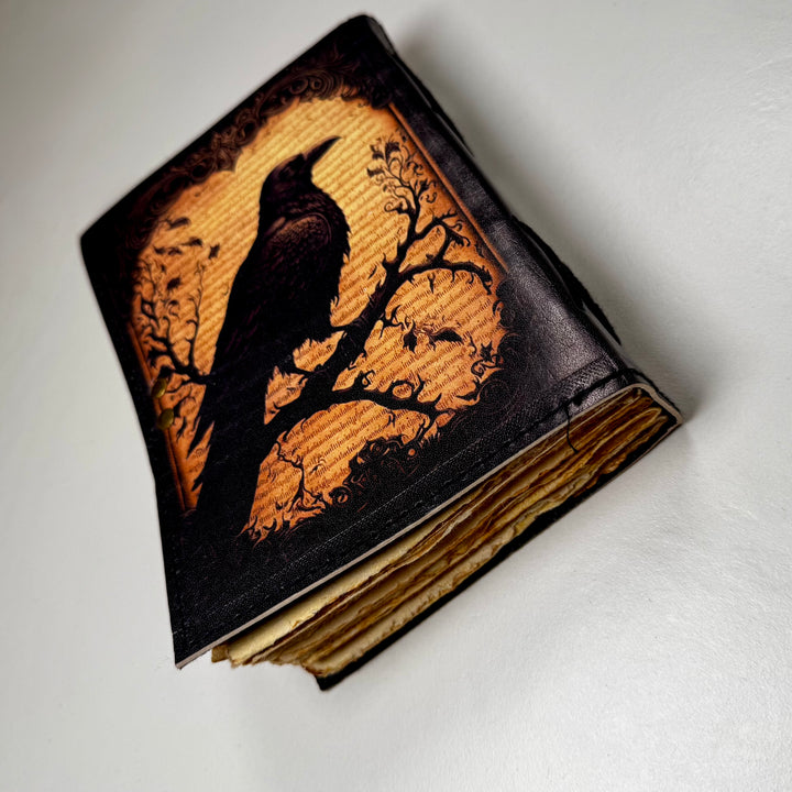 Korppiaiheinen nahkakantinen muistikirja takaa kuvattuna, esillä kirjan paksuus ja takakansi. - Raven-themed leather-bound journal photographed from the back, showing the book’s thickness and back cover.