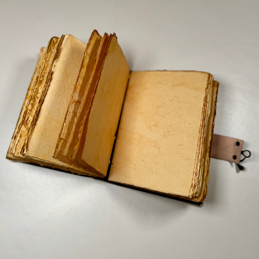 Käsintehty nahkainen muistikirja avattuna – näkyvissä sivuaukeama ja käsintehdyn paperin rustiikkinen tekstuuri. - Handcrafted leather notebook opened – showing a double page spread with the rustic texture of handmade paper.