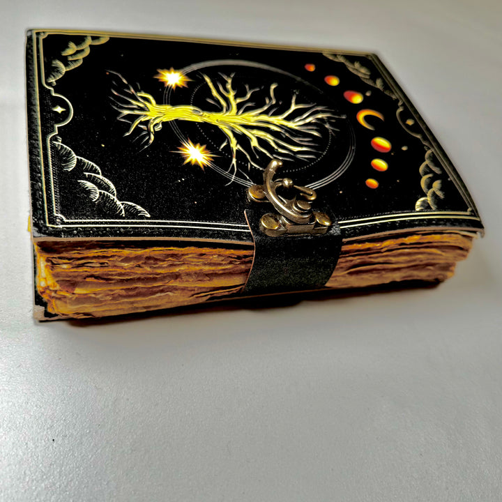 Elämänpuu-aiheinen nahkakantinen muistikirja sivusta kuvattuna, esillä kirjan paksuus ja lukko. - Tree of Life -themed leather-bound notebook photographed from the side, showing the book’s thickness and lock.