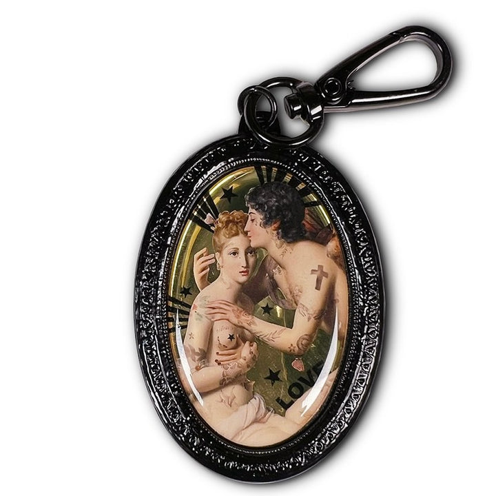 Ovaalinmuotoinen avaimenperä, jossa kehystetty kuva François Gérardin maalauksesta "Cupid ja Psyche" (1798), Voglio Benen uudelleentulkinta tatuoinnein ja modernin graafisin elementein. - Oval keychain with a framed image inspired by François Gérard’s painting "Cupid and Psyche" (1798), reinterpreted with tattoos and modern graphic elements by Voglio Bene.