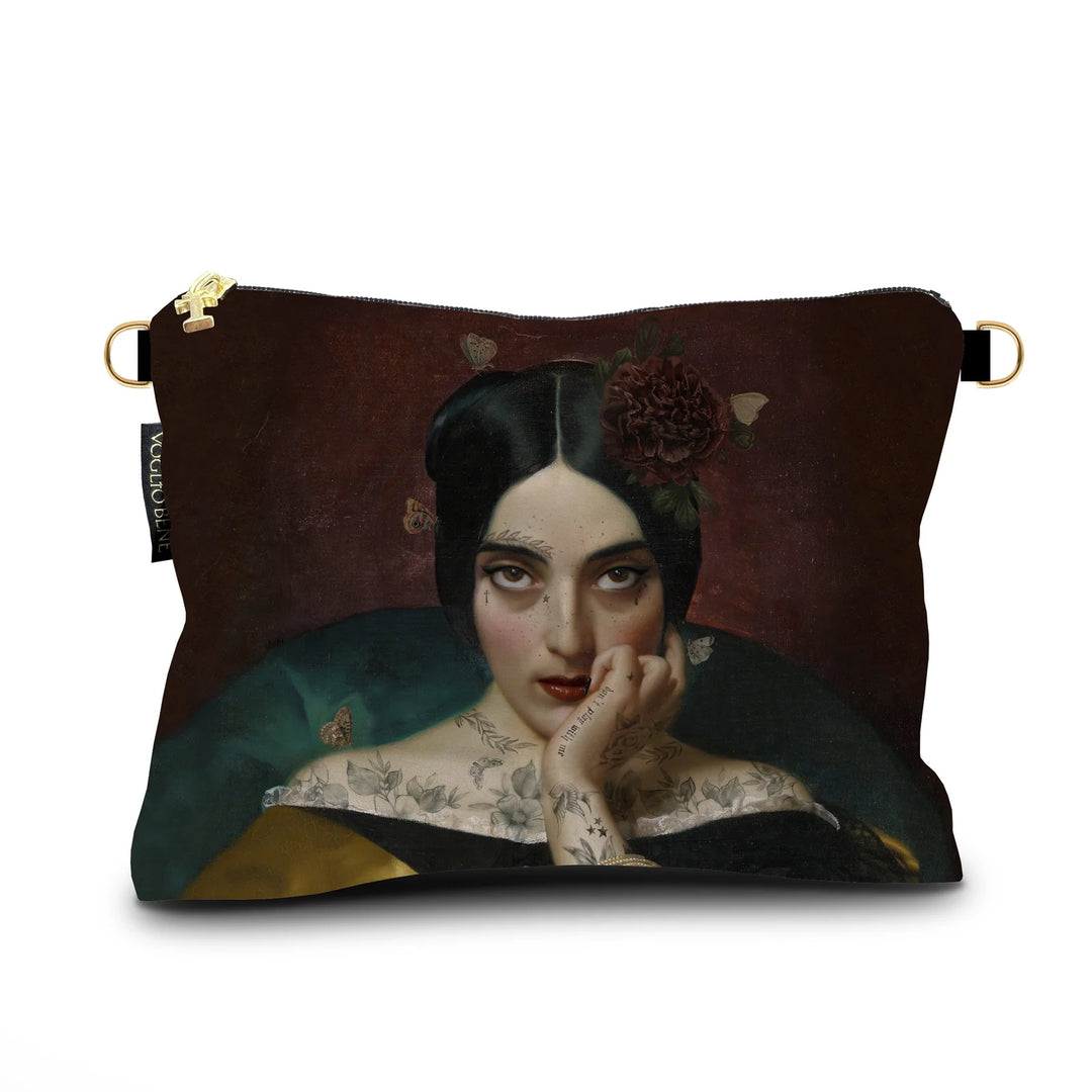 Kuvassa Voglio Bene samettilaukun etupuoli Clementine -kuvituksella, jossa tatuoitu nainen tummanpunaisella taustalla katsoo intensiivisesti kohti katsojaa.
In the image, the front side of a Voglio Bene velvet bag with the Clementine illustration, depicting a tattooed woman on a dark red background gazing intensely at the viewer.