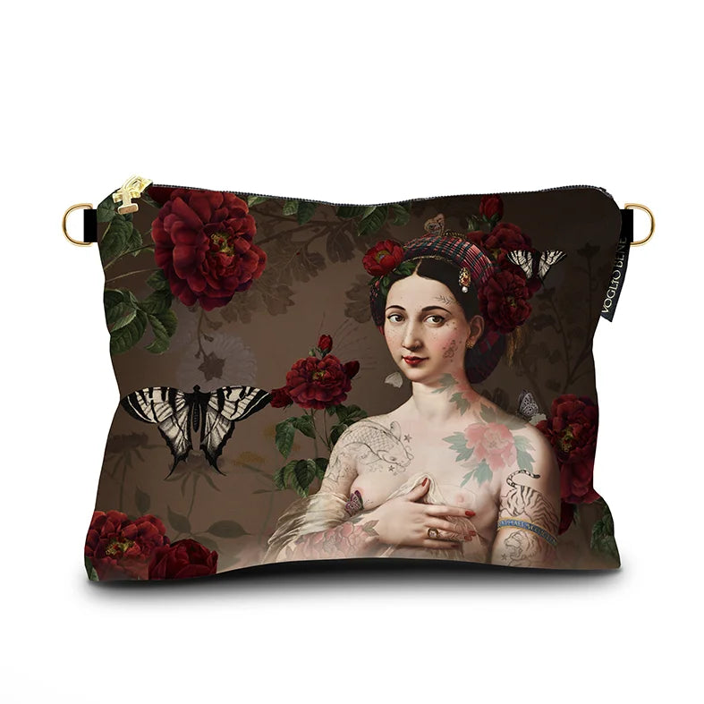 Kuvassa Voglio Bene -samettilaukku Fornarina -kuvituksella. Tatuoitu nainen kukkia hiuksissaan ruskealla taustalla, ympärillään kukkia ja perhosia.
The Voglio Bene velvet bag with Fornarina illustration. A tattooed woman with flowers in her hair against a brown background, surrounded by flowers and butterflies.