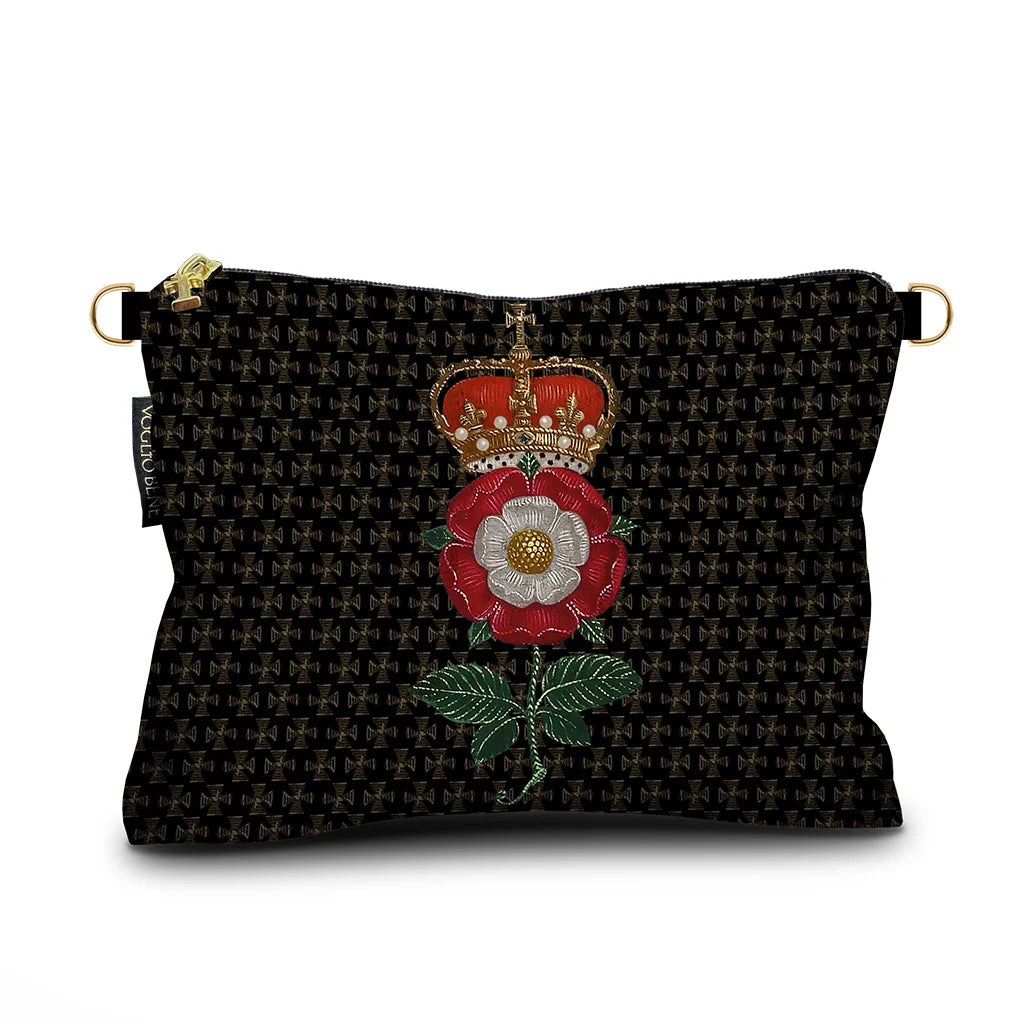 Kuvassa Voglio Bene -samettilaukku Notre Dame -kuvituksella. Punavalkoinen kukka, jonka päällä on kruunu, erottuu tummalla geometrisella taustalla.
The Voglio Bene velvet bag with Notre Dame illustration. A red and white flower crowned with a golden crown stands out against a dark geometric background.