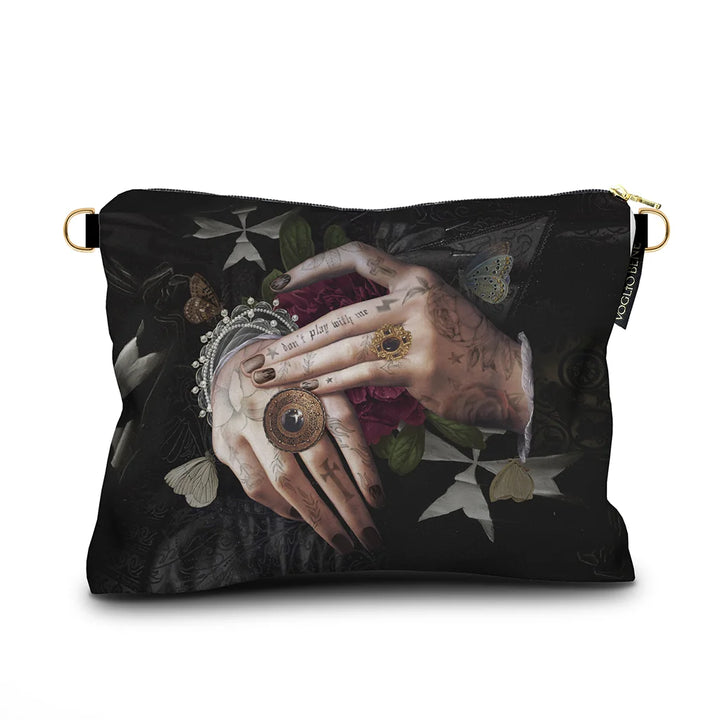 Kuvassa Voglio Bene -samettilaukku Protection -kuvituksella. Tatuoidut kädet lepäävät limittäin, sormissa tummia sormuksia ja käsien alla punainen kukka, taustana tumma goottinen kuviointi.
The Voglio Bene velvet bag with Protection illustration. Tattooed hands rest intertwined, adorned with dark rings, with a red flower beneath them against a dark gothic background.