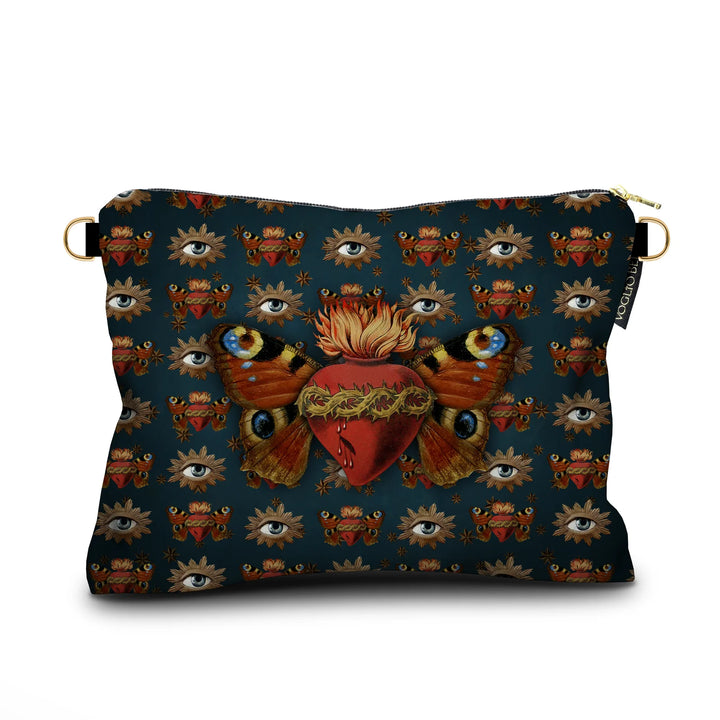 Kuvassa Voglio Bene -samettilaukku Sacred Butterfly -kuvituksella. Sydän, jota puristavat orjantappurat, liekehtii yläosastaan ja sillä on perhosen siivet. Taustalla sinisellä pohjalla vuorottelevat sama sydänkuvio ja säteilevä silmä.
The Voglio Bene velvet bag with Sacred Butterfly illustration. A heart encircled by thorns emits flames from its top and has butterfly wings. The blue background alternates between the same heart motif and a radiant eye.