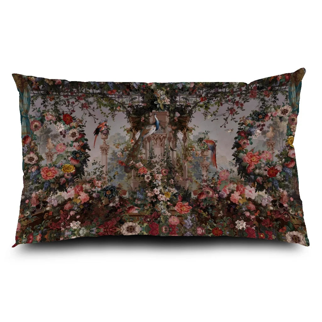 Voglio Bene Paradise -tyynyn etunäkymä. Kuvassa roomalaistyylinen gazebo, jota ympäröivät kukat, riikinkukot sekä trooppiset linnut rehevässä puutarhassa.
Front view of a Voglio Bene Paradise cushion. The illustration shows a Roman-style gazebo surrounded by flowers, peacocks, and tropical birds in a lush garden.