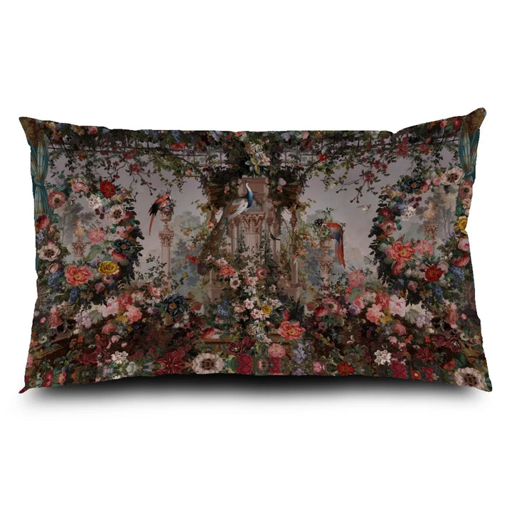 Voglio Bene Paradise -tyynyn etunäkymä. Kuvassa roomalaistyylinen gazebo, jota ympäröivät kukat, riikinkukot sekä trooppiset linnut rehevässä puutarhassa.
Front view of a Voglio Bene Paradise cushion. The illustration shows a Roman-style gazebo surrounded by flowers, peacocks, and tropical birds in a lush garden.