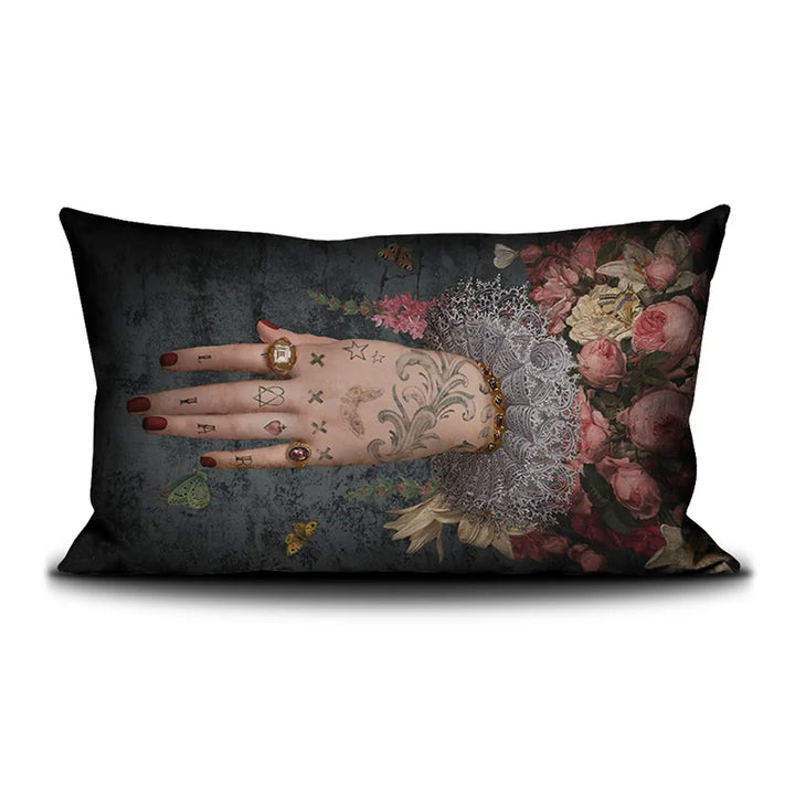 Voglio Bene Poderosa -tyynyn etunäkymä. Kuvassa yksi tatuoitu käsi osoittaa vasemmalle kukkaornamenttien keskeltä.
Front view of a Voglio Bene Poderosa cushion. The image features a single tattooed hand pointing to the left among floral ornaments.