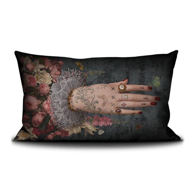 Voglio Bene Poderosa -tyynyn etunäkymä. Kuvassa yksi tatuoitu käsi osoittaa oikealle kukkaornamenttien keskeltä.
Front view of a Voglio Bene Poderosa cushion. The image features a single tattooed hand pointing to the right among floral ornaments.