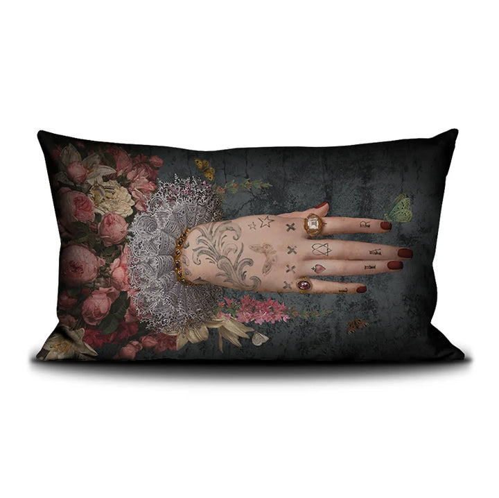 Voglio Bene Poderosa -tyynyn etunäkymä. Kuvassa yksi tatuoitu käsi osoittaa oikealle kukkaornamenttien keskeltä.
Front view of a Voglio Bene Poderosa cushion. The image features a single tattooed hand pointing to the right among floral ornaments.