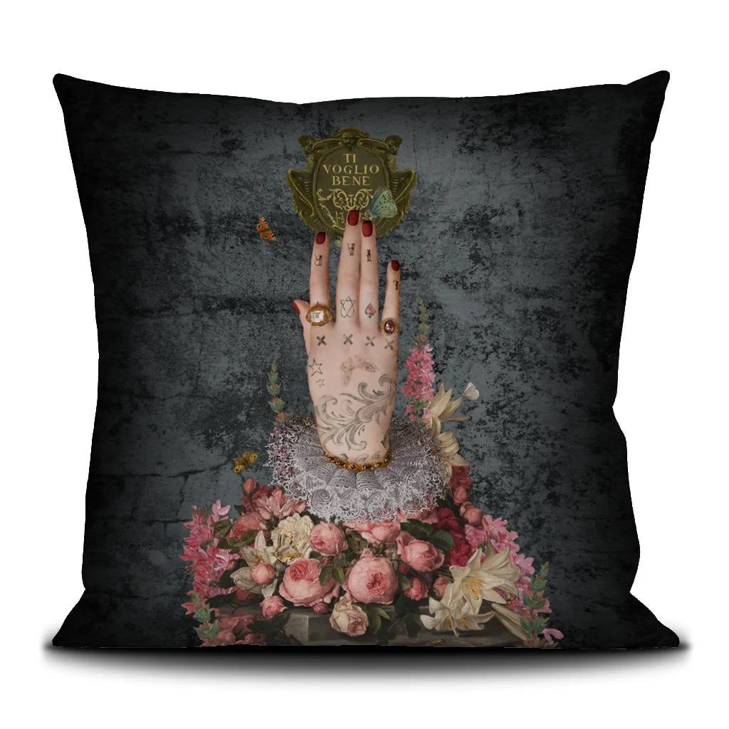 Voglio Bene Poderosa -tyynyn etunäkymä. Kuvassa yksi tatuoitu käsi osoittaa suoraan ylöspäin kukkaornamenttien keskeltä.
Front view of a Voglio Bene Poderosa cushion. The image features a single tattooed hand pointing straight upward among floral ornaments.