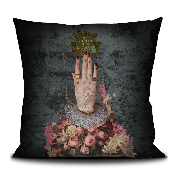 Voglio Bene Poderosa -tyynyn etunäkymä. Kuvassa yksi tatuoitu käsi osoittaa suoraan ylöspäin kukkaornamenttien keskeltä.
Front view of a Voglio Bene Poderosa cushion. The image features a single tattooed hand pointing straight upward among floral ornaments.