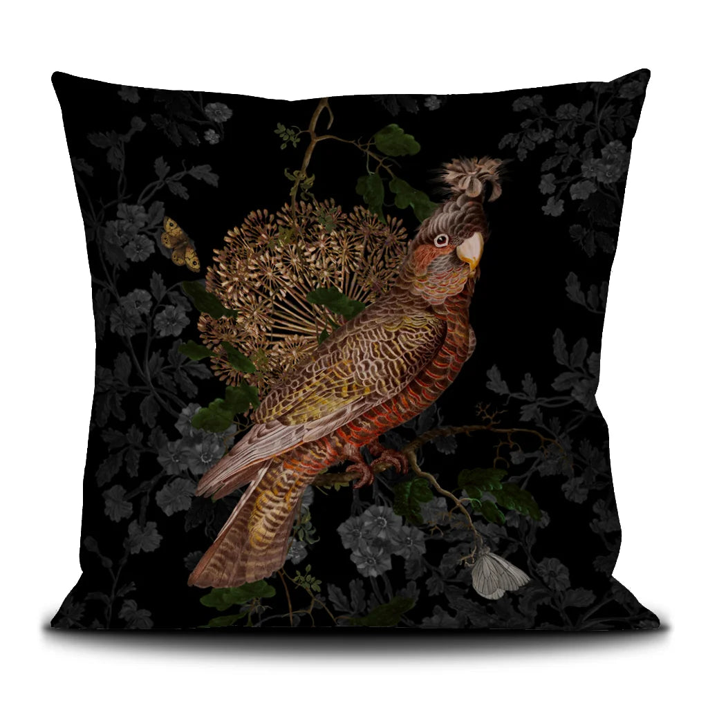 Kuvassa Voglio Bene -tyyny Rio -kuvituksella. Papukaija ja perhonen erottuvat mustalla metsätaustalla.
The Voglio Bene cushion with Rio illustration. A parrot and a butterfly stand out against a dark forest background.