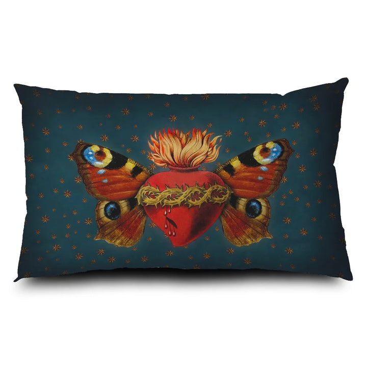 Kuvassa Voglio Bene -tyyny Sacred Butterfly -kuvituksella. Sydän, jota puristavat orjantappurat, liekehtii yläosastaan ja sillä on perhosen siivet. Taustalla sinisellä pohjalla tähtikuvioita.
The Voglio Bene cushion with Sacred Butterfly illustration. A heart encircled by thorns emits flames from its top and has butterfly wings. The blue background has starry ornaments.