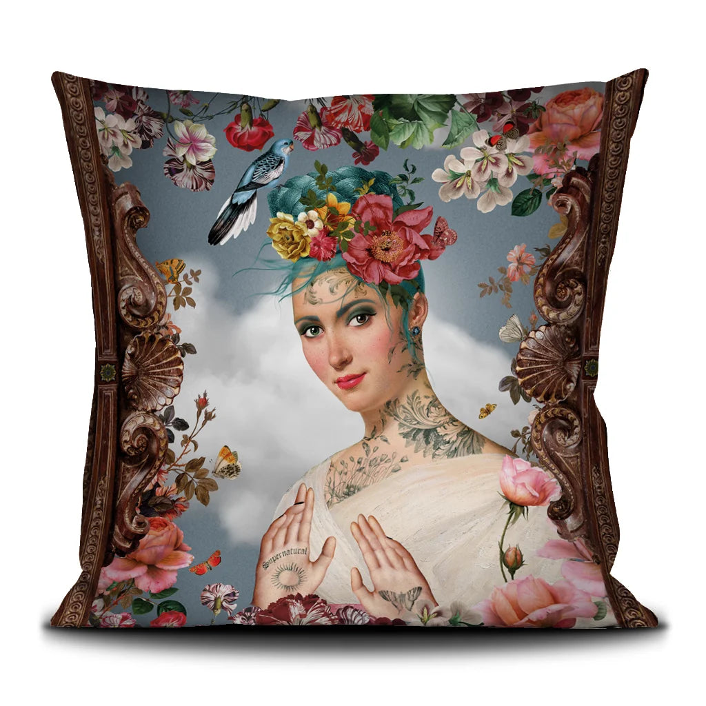 Voglio Bene Spring -tyynyn etunäkymä, jossa sinihiuksinen tatuoitu nainen on kuvattu lintu ja kukkia hiuksissaan.
Front view of a Voglio Bene Spring cushion, showing a blue-haired tattooed woman with a bird and flowers in her hair.
