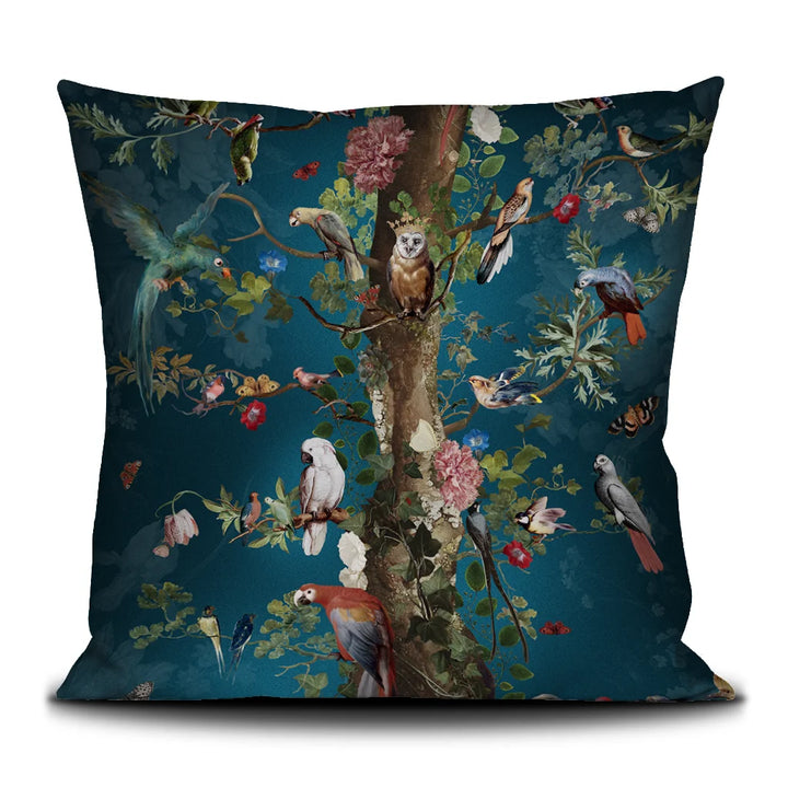 Kuvassa Voglio Bene tyynyn etunäkymä Tree of Life -kuvituksella. Puu kohoaa sinisellä taustalla, sen oksalla istuu kruunupäinen pöllö ja ympärillä on runsaasti trooppisia lintuja.
The front view off Voglio Bene cushion with Tree of Life illustration. A tree rises against a blue background, with an owl wearing a crown perched on a branch, surrounded by tropical birds.