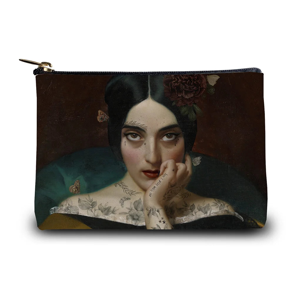 Kuvassa Voglio Bene kukkaron etupuoli Clementine -kuvituksella, jossa tatuoitu nainen tummanpunaisella taustalla katsoo intensiivisesti kohti katsojaa.
In the image, the front side of a Voglio Bene purse with the Clementine illustration, depicting a tattooed woman on a dark red background gazing intensely at the viewer.