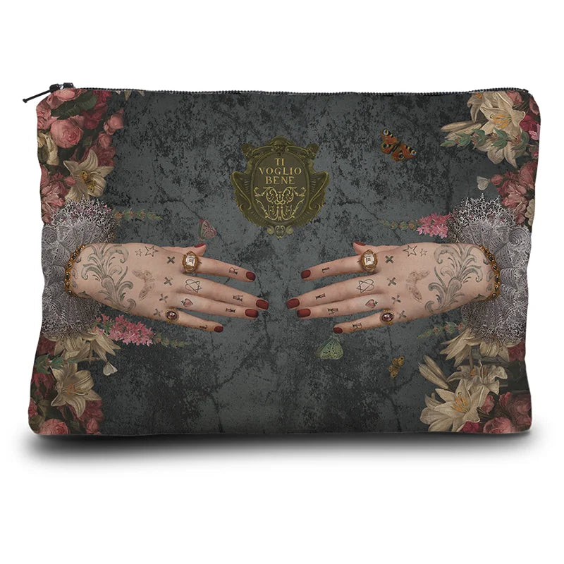 Voglio Bene Poderosa -kukkaron takanäkymä. Kuvassa kaksi tatuoitua, sormuksilla koristeltua kättä osoittavat toisiaan kukkien reunustamana.
Back view of a Voglio Bene Poderosa purse. The illustration shows two tattooed hands adorned with rings, pointing toward each other, framed by flowers.