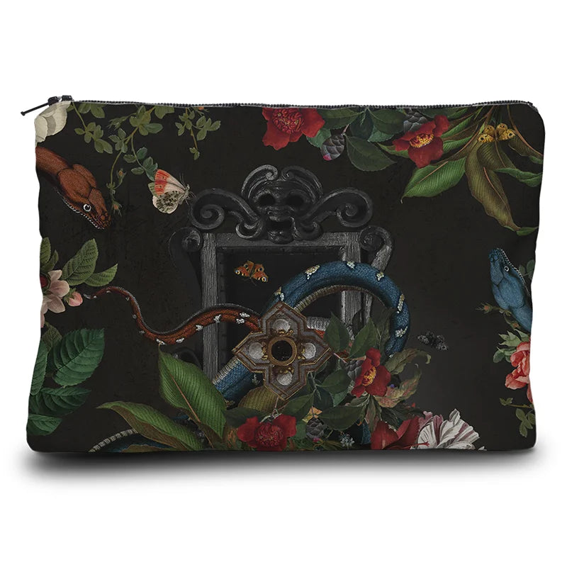 Kuvassa Voglio Bene kukkaron takapuoli Turmoil -kuvituksella, jossa tumma peili on kukkien ja käärmeiden ympäröimänä.
In the image, the back side of a Voglio Bene purse with the Turmoil illustration, showing a dark mirror framed by flowers and snakes.
