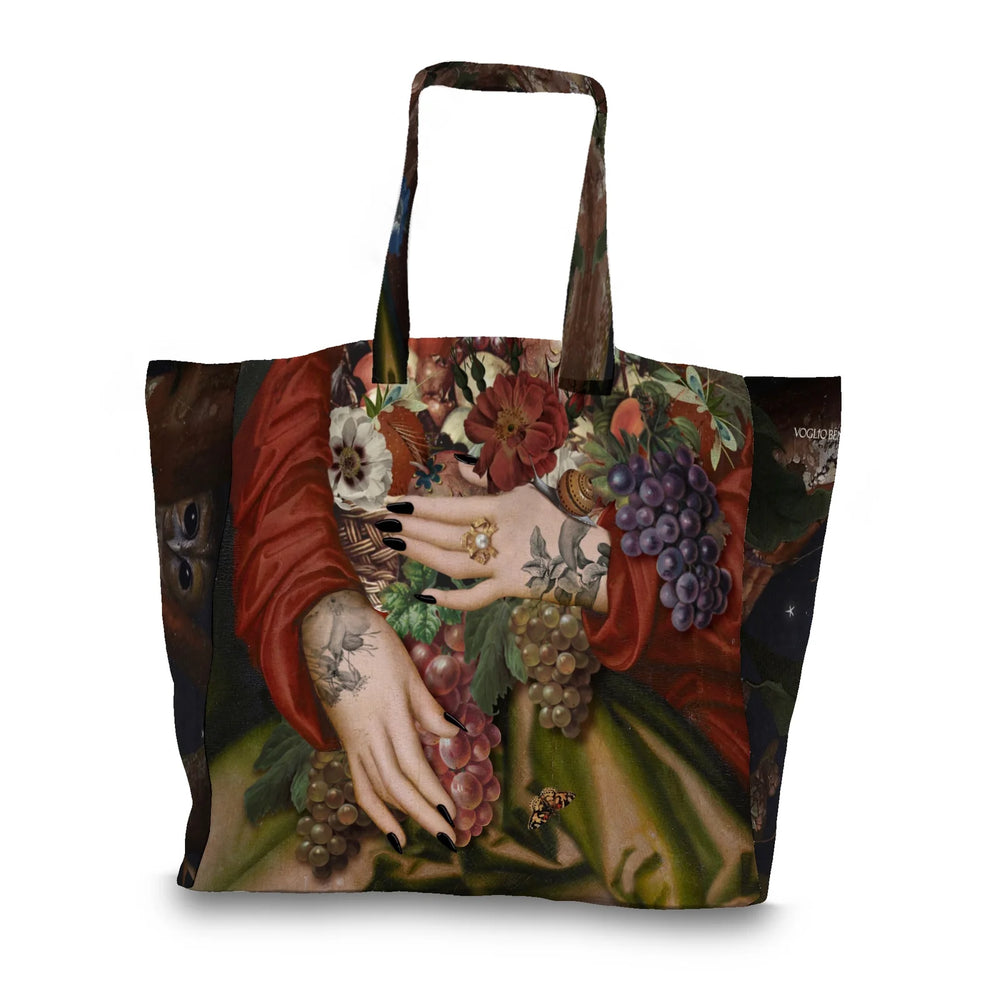Kuvassa Voglio Bene tote bagin takapuoli Autumn-kuvituksella. Tatuoidut kädet pitelevät runsasta kukista ja hedelmistä koostuvaa asetelmaa.
The back of the Voglio Bene tote bag with Autumn illustration. Tattooed hands hold a rich arrangement of flowers and fruits.