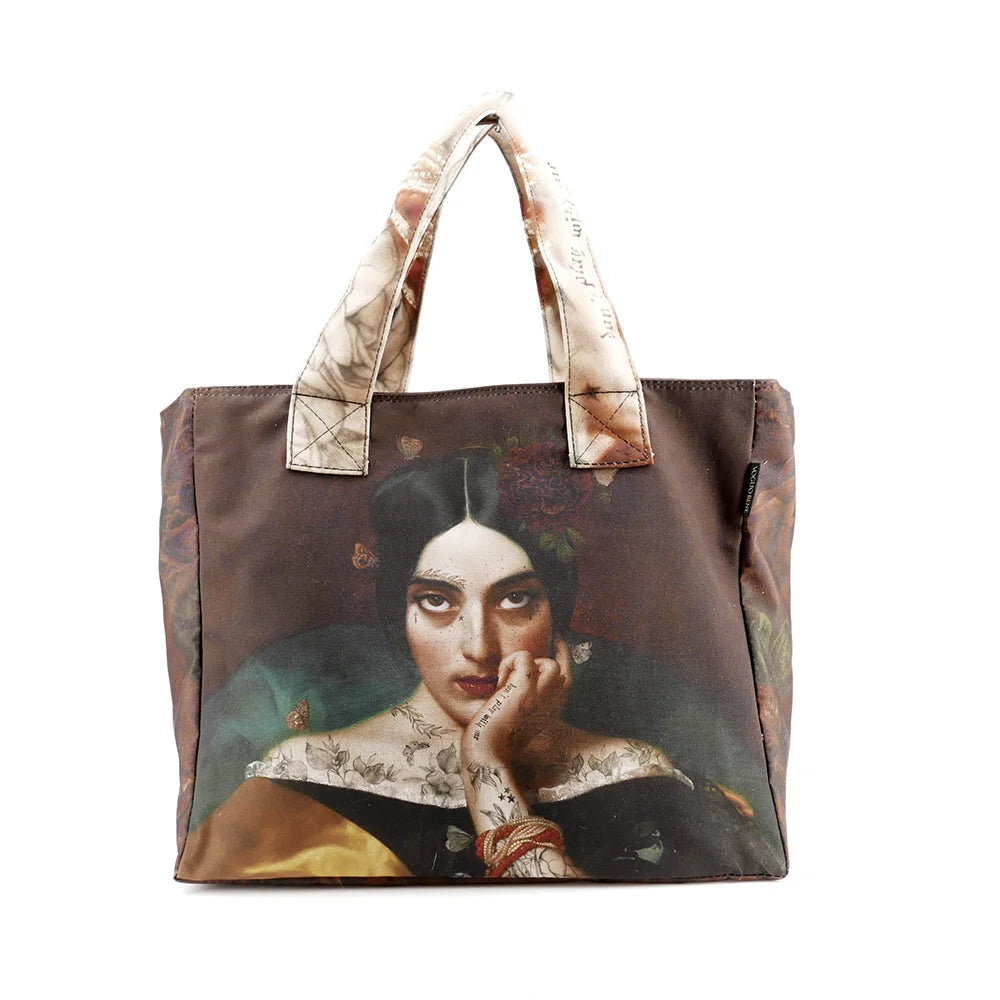 Kuvassa Voglio Bene tote bag etupuoli Clementine -kuvituksella, jossa tatuoitu nainen tummanpunaisella taustalla katsoo intensiivisesti kohti katsojaa.
In the image, the front side of a Voglio Bene tote bag with the Clementine illustration, depicting a tattooed woman on a dark red background gazing intensely at the viewer.