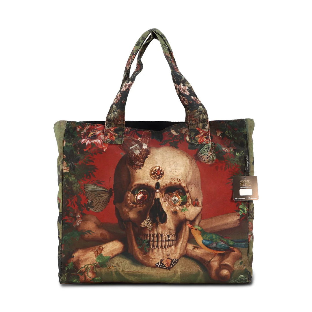 Kuvassa Voglio Bene tote bag etupuoli Eternity -kuvituksella, jossa pääkallon silmistä roikkuu kimaltavia koruja, ja punaista taustaa koristavat linnut, kasvit ja perhoset.
In the image, the front side of a Voglio Bene tote bag with the Eternity illustration, showing a skull with sparkling jewelry hanging from its eyes, surrounded by birds, plants, and butterflies on a red background.