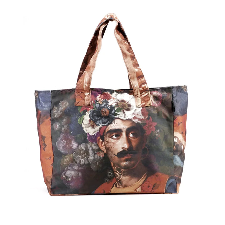 Kuvassa Voglio Bene tote bag etupuoli Hassan -kuvituksella, jossa viiksekäs tatuoitu mies kukkaturbaani päässä on kuvattuna tummanvihreällä taustalla, joka on täynnä kukkia.
In the image, the front side of a Voglio Bene tote bag with the Hassan illustration, featuring a mustached tattooed man wearing a floral turban against a dark green flower-filled background.
