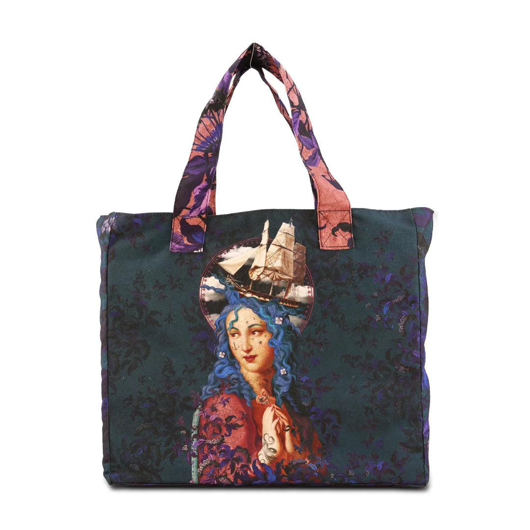 Kuvassa Voglio Bene -tote bag Holy Storm -kuviolla. Tatuoitu sinihiuksinen nainen seisoo sinivioletin ornamenttitaustan edessä, sädekehän ympärillä näkyy vettä, myrsky ja kamppailualus.
The Voglio Bene tote bag with Holy Storm illustration. A tattooed blue-haired woman stands against a blue-purple ornamental background, surrounded by water, a storm, and a warship in her halo.