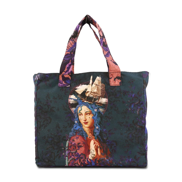 Kuvassa Voglio Bene -tote bag Holy Storm -kuviolla. Tatuoitu sinihiuksinen nainen seisoo sinivioletin ornamenttitaustan edessä, sädekehän ympärillä näkyy vettä, myrsky ja kamppailualus.
The Voglio Bene tote bag with Holy Storm illustration. A tattooed blue-haired woman stands against a blue-purple ornamental background, surrounded by water, a storm, and a warship in her halo.