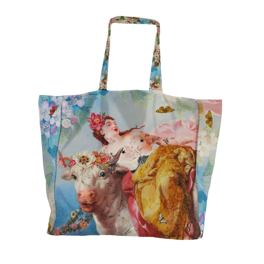 Voglio Bene Cow -tote bag etunäkymä, jossa lehmä ja tatuoitu nainen on kuvattu yhdessä kukkaornamentein koristeltuna.
Front view of a Voglio Bene Cow tote bag,  showing a cow together with a tattooed woman adorned with floral ornaments.