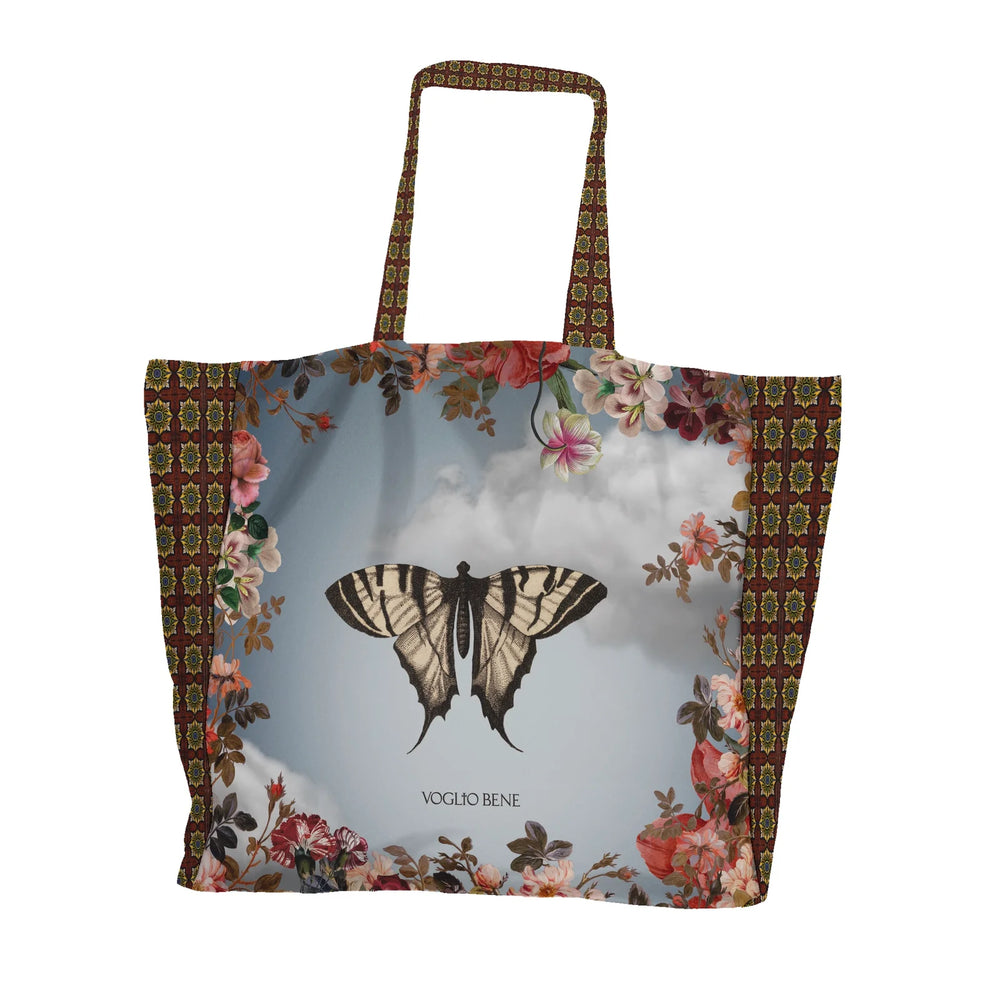 Kuvassa Voglio Bene tote bagin takapuoli The Spring -kuvituksella. Mustavalkoinen perhonen sinisellä taivaalla kukkien reunustamana.
The back of the Voglio Bene tote bag with The Spring illustration. A black and white butterfly against a blue sky framed by flowers.