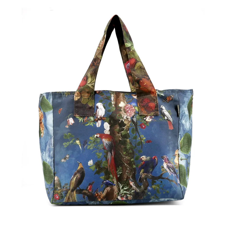 Kuvassa Voglio Bene tote bagin takapuoli Tree of Life -kuvituksella. Puu jatkuu sinisellä taustalla, ja sen oksilla istuu papukaijoja ja muita trooppisia lintuja.
The back of the Voglio Bene tote bag with Tree of Life illustration. The tree continues against a blue background, with parrots and tropical birds perched on its branches.