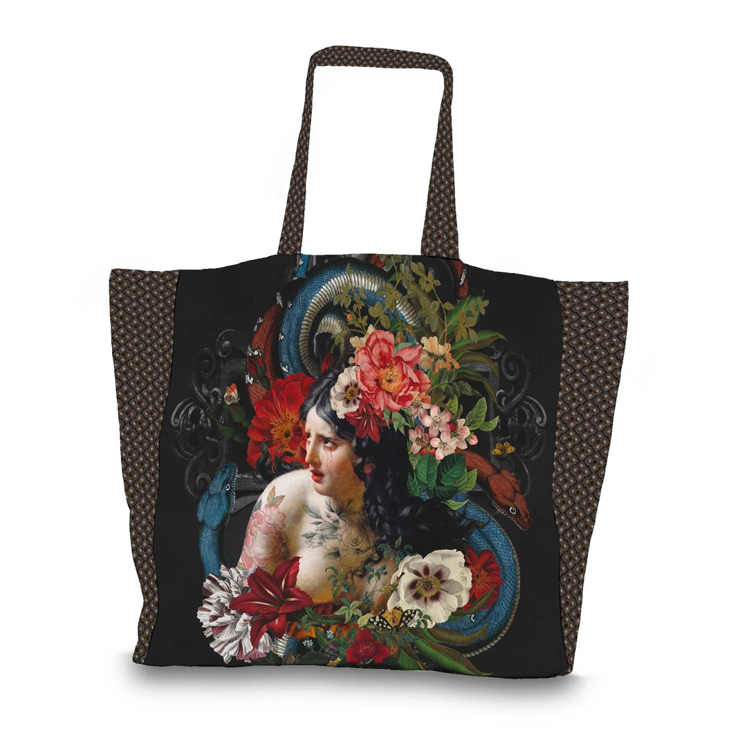 Kuvassa Voglio Bene tote bag etupuoli Turmoil -kuvituksella, jossa itkevä tatuoitu nainen on kuvattuna kukkien ja käärmeiden ympäröimänä tummalla taustalla.
In the image, the front side of a Voglio Bene tote bag with the Turmoil illustration, depicting a crying tattooed woman surrounded by flowers and snakes against a dark background.