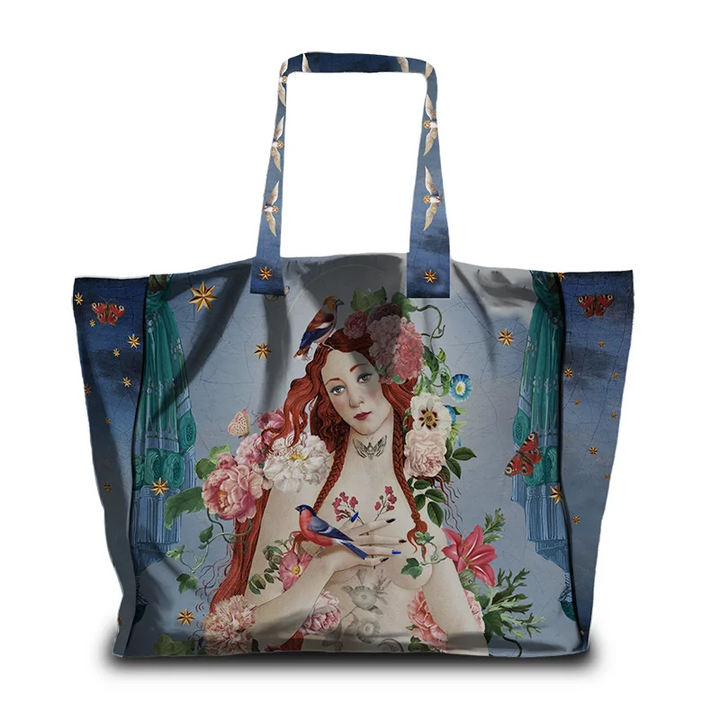 Kuvassa Voglio Bene tote bag etupuoli Venus Gypsy -kuvituksella, jossa lintuja istuu punahiuksisen naisen päällä kukkien ympäröimänä sinisellä taustalla.
In the image, the front side of a Voglio Bene tote bag with the Venus Gypsy illustration, showing birds sitting on a red-haired woman surrounded by flowers with a blue backround. 