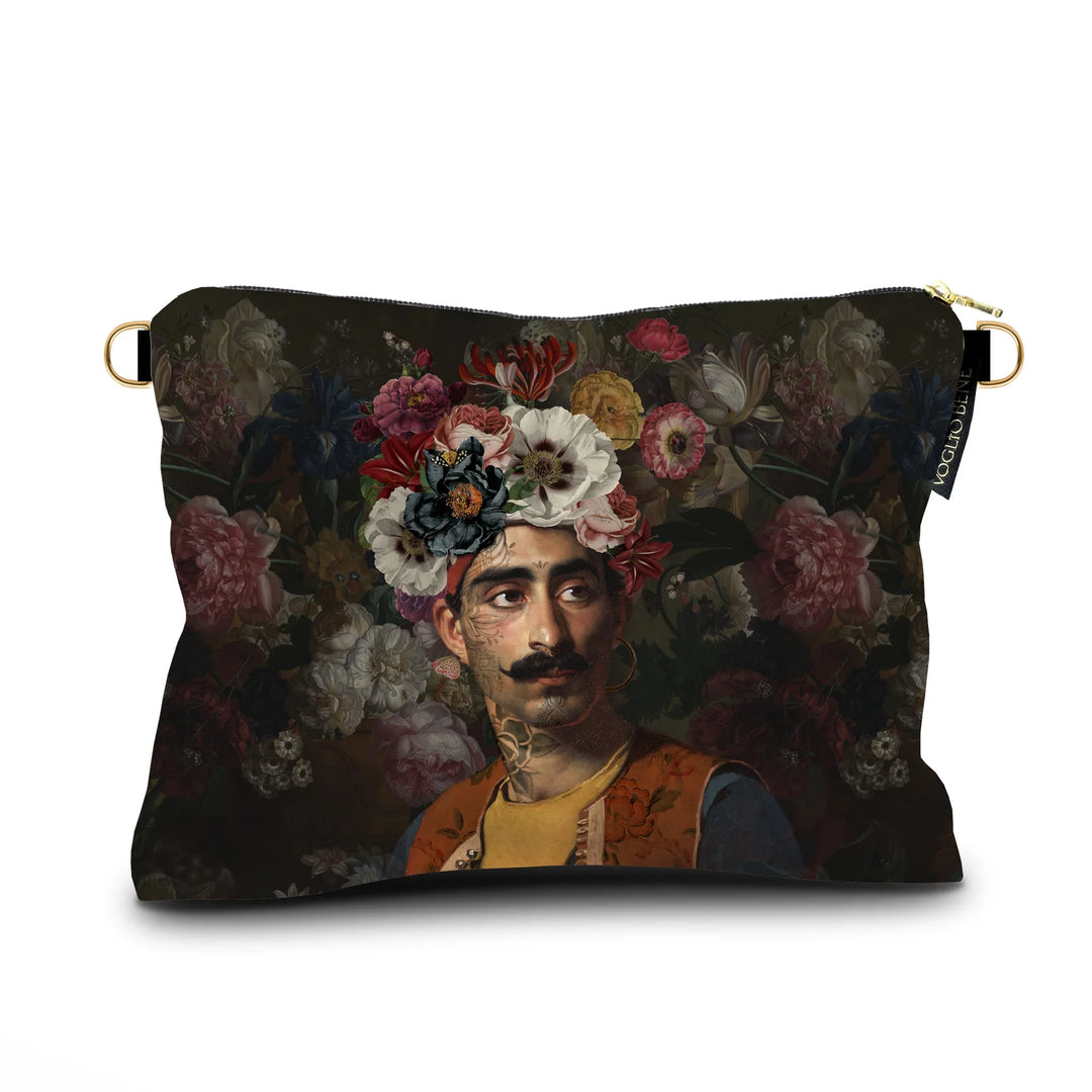 Kuvassa Voglio Bene samettilaukun etupuoli Hassan -kuvituksella, jossa viiksekäs tatuoitu mies kukkaturbaani päässä on kuvattuna tummanvihreällä taustalla, joka on täynnä kukkia.
In the image, the front side of a Voglio Bene velvet bag with the Hassan illustration, featuring a mustached tattooed man wearing a floral turban against a dark green flower-filled background.