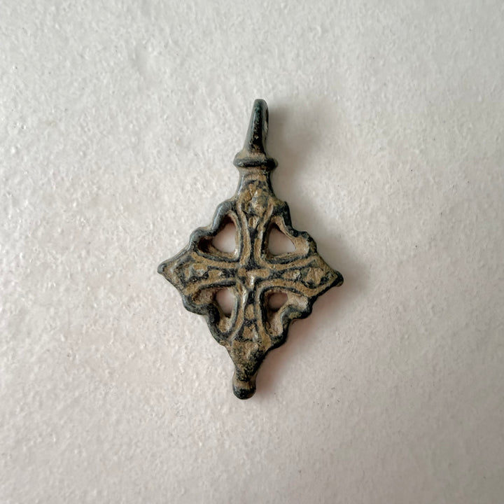 Viikinkiaikainen pronssinen ristiriipus, etupuoli, avoin kehyksellinen risti vihertävänruskealla patinalla - Viking Age bronze cross pendant, front view, openwork framed cross with greenish-brown patina.