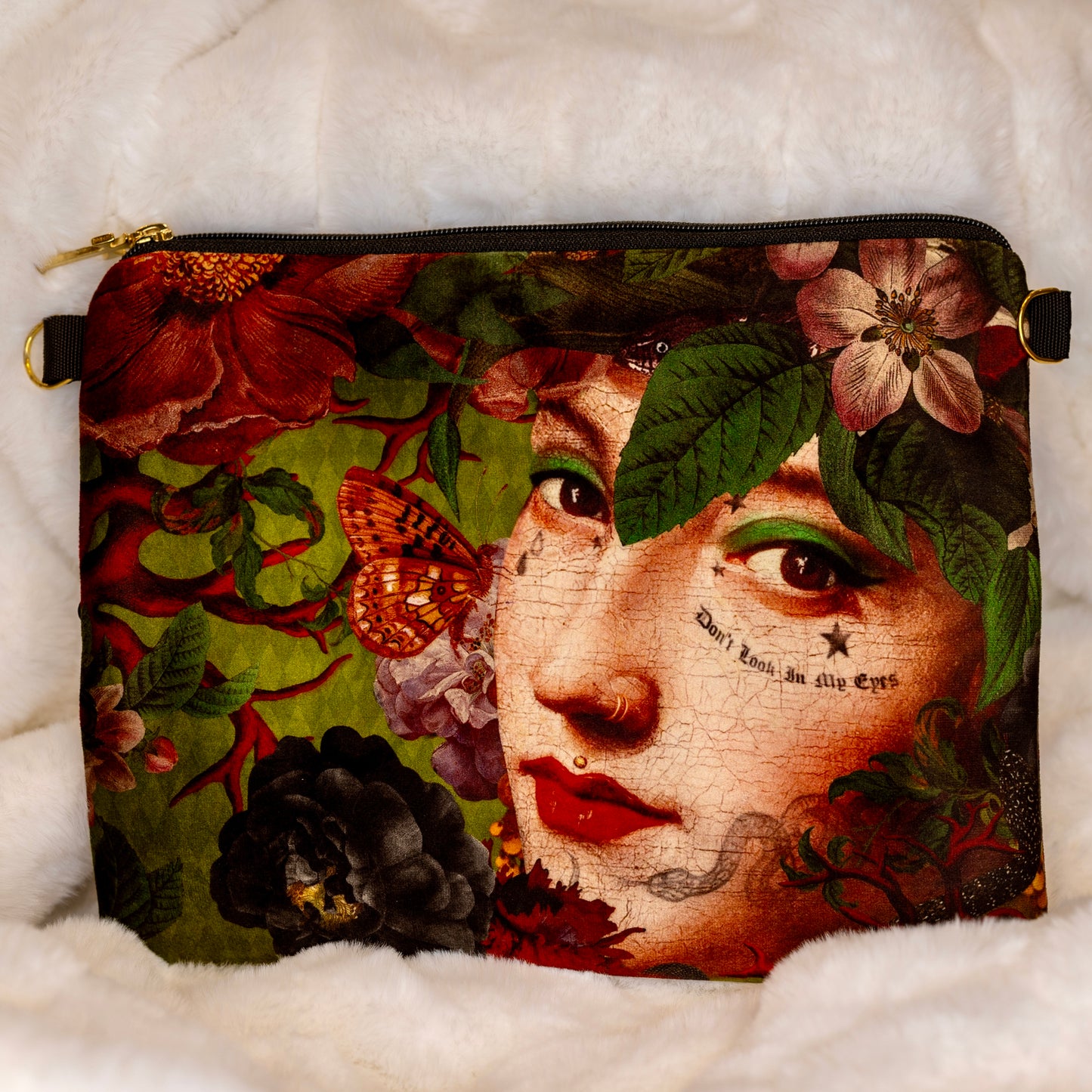 Voglio Benen samettipussukka, jossa Meduusan kasvokuva kukkien ja lehtien peittämänä. Teksti 'Don’t look in the eyes' tuo modernin vivahteen myyttiseen hahmoon. - Voglio Bene velvet pouch featuring a detailed print of Medusa's face covered with flowers and leaves. The text 'Don't look in the eyes' adds a modern twist to the mythical figure.