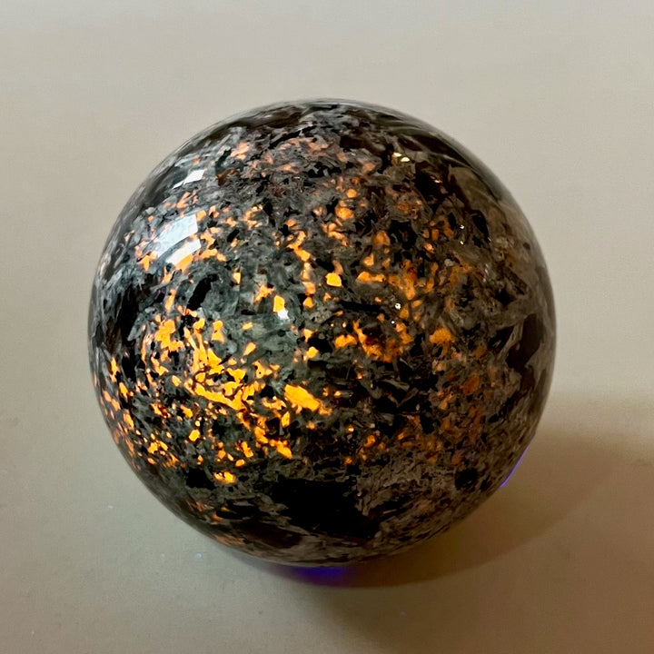 Yooperlite-pallo hehkuu kirkkaan oranssina UV-valossa. - Yooperlite sphere glowing bright orange under UV light.