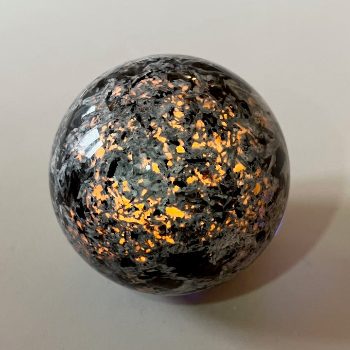 Pyöreä Yooperlite-kivi säihkyy oranssina UV-lampun alla. - Round Yooperlite stone glowing orange under UV lamp.