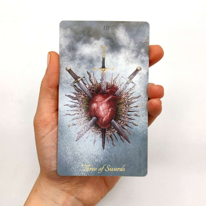 Baroque Tarot -pakan Three of Swords -kortti kädessä.