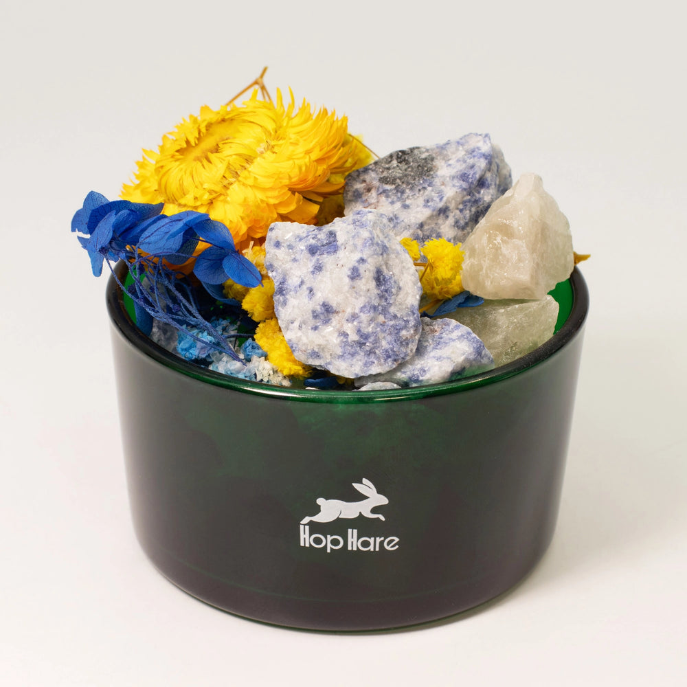Hop Hare The Sun crystal diffuser in a dark green glass vessel with sodalite and blue and yellow dried flowers.