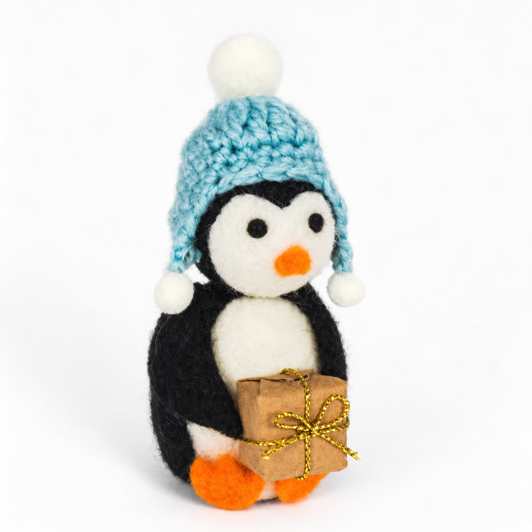 Felt penguin in a blue bobble hat holding a brown gift parcel tied with a gold-coloured ribbon.