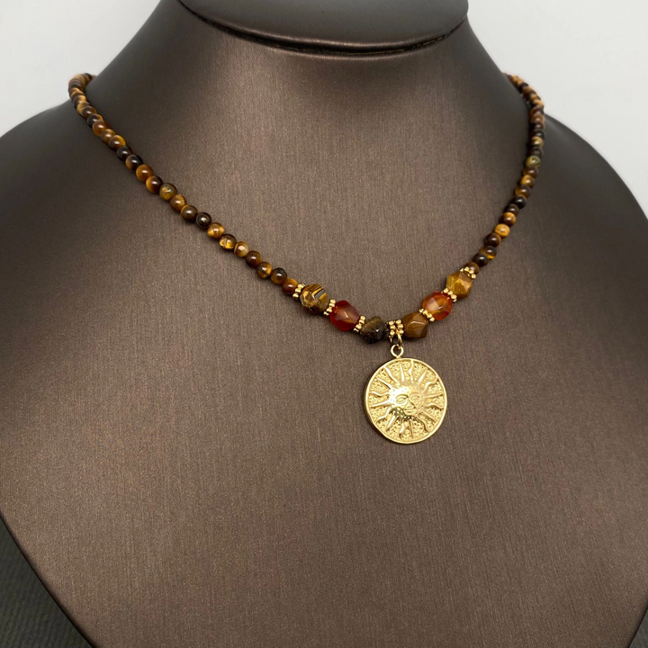Tiger’s eye necklace with faceted beads and a gold-coloured sun pendant on a dark jewellery display bust.
