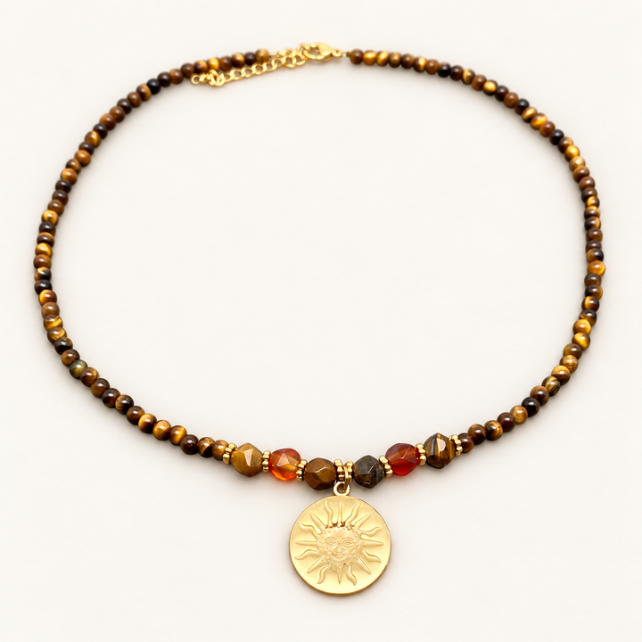 Tiger’s eye beaded necklace with a gold-coloured sun pendant on a soft, pale background.