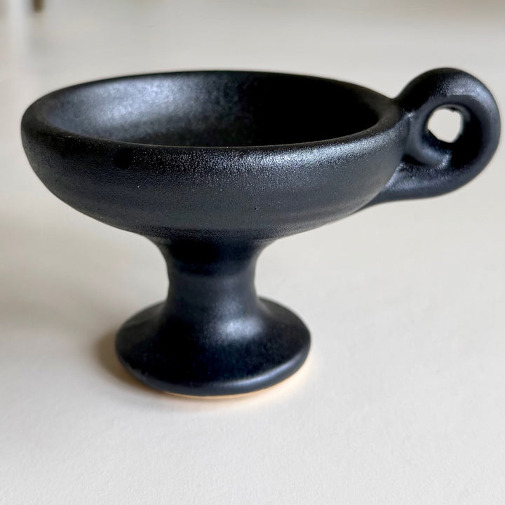 Black ceramic incense burner with a pedestal base and ring handle, viewed from the side.